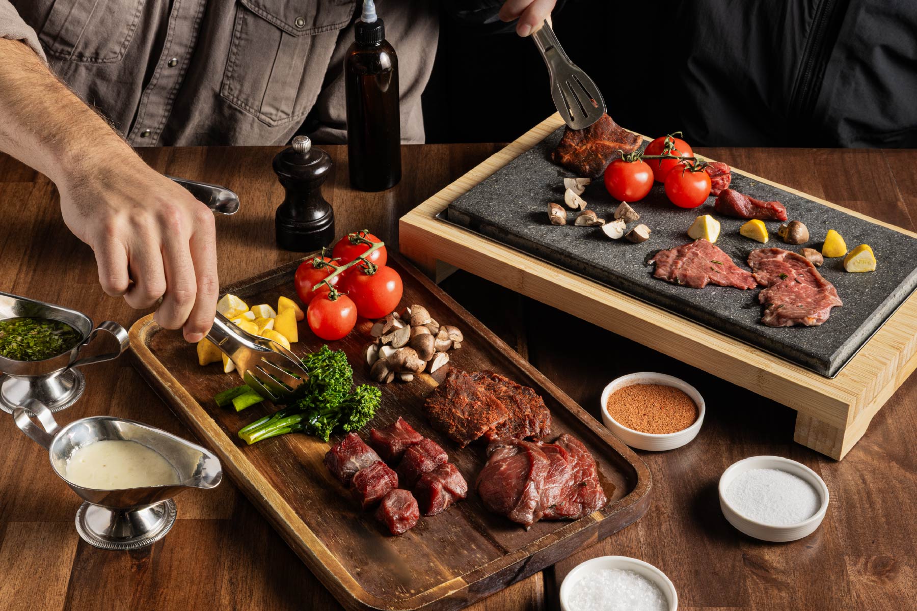 Steak and vegetables on wooden boards, with sauces on a table.